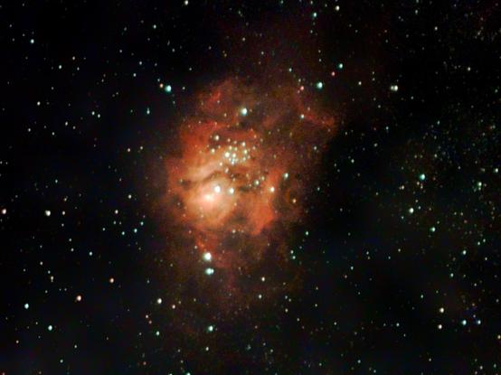 An orange-red nebula against a dark sky. There are many bright stars in the nebula.