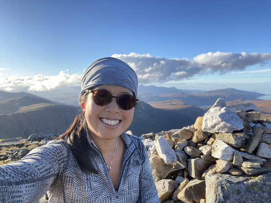 Grinning author at summit cairn in front of mountains