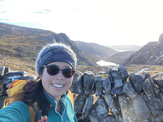 Smiling author in front of dry stone wall, mountains in background
