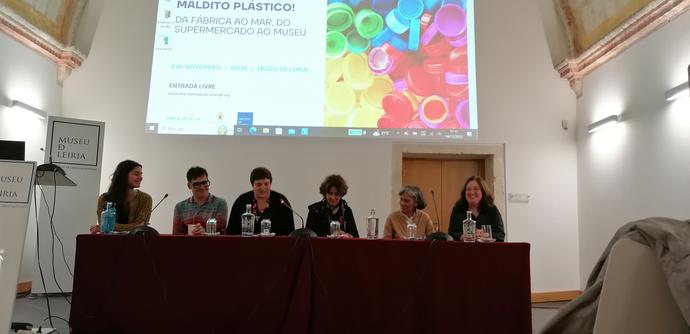 Mesa de dabate no final do dia da ComceptCon, com todas as oradoras (Joana Tomás, Paula Sobral, Ana Barros e Paula Quinteiro) e o artista Nuno Sousa Viiera. A moderar, estava a Vânia Carvalho, coordenadora do Museu de Leiria. Por trás da mesa, projectado na parede, vê-se o cartaz da ComceptCon 2023, com o título, data, local e uma fotografia de muitas tampas de plástico de diversas cores — a imagem representativa da ComceptCon deste ano.