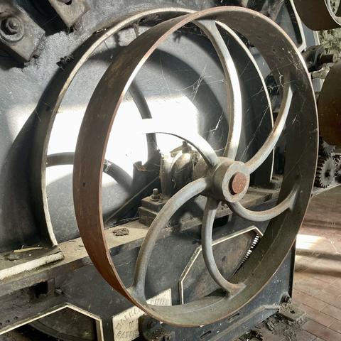 Large metal wheel as part of a mill machine. Grey and some red rust.