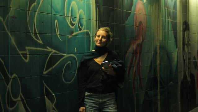 Eine Frau steht mit dem Smartphone vor einem Grafitti.