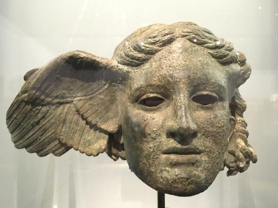 Visage en bronze, de face, représentant Hypnos, le dieu grec du sommeil. 
Il est le frère jumeau de Thanatos qui, lui, personnifie la mort. 
Deux ouvertures en forme d'amande sont à la place des yeux, sous les paupières, comme sur un masque. 
Depuis la tempe droite de ce visage se déploie une aile.