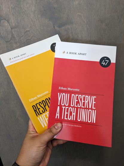 My hand holding two books: the red "You Deserve a Tech Union" in front, and the yellow "Responsive Web Design" behind.