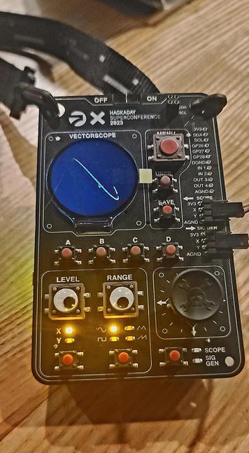 Front of badge with circular display, googly eye buttons, and many switches.
