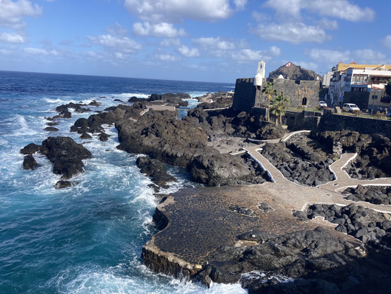 Rocky paths over old lava flow with rough sea blue sky white clouds and old stone building