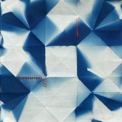 A mix of squares and triangles in an unbalanced geometric pattern in blue and white, on paper that shows the folds from previously being an origami form. There is red stitching mending small rips in the paper