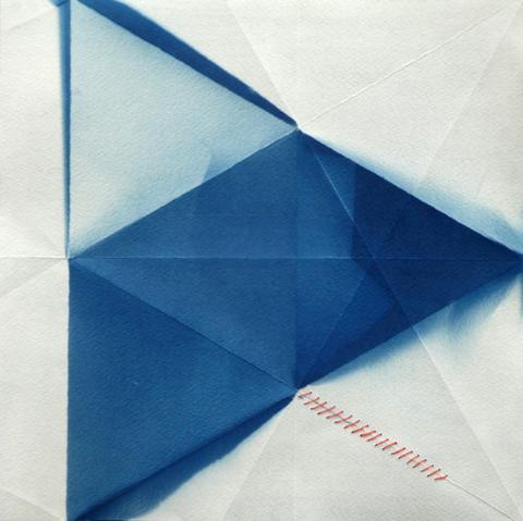 A triangular unbalanced geometric pattern in blue and white, on paper that shows the folds from previously being an origami form. There is red stitching mending small rips in the paper. One large triangle is made of four smaller equilateral triangles