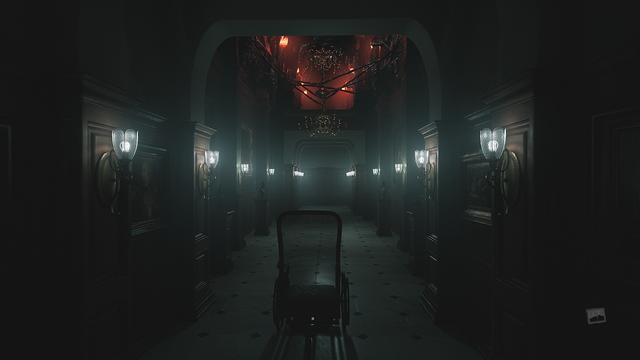 Zrzut ekranu z gry "Layers of Fear" przedstawiający korytarz-galerię, oświetloną trupio-bladym światłem, wydobywającą się z rzędów miedzianych klinkietów w kształcie tulipanów po obu stronach przejścia, oraz niepokojącym, czerwono-pomarańczowym światłem przywodzącym na myśl szalejący ogień, dobywającym się z ozdobnego, mosiężnego żyrandola zwisającego pośrodku korytarza ze sznurów czarnej, bezkształtnej masy zarastającej pustą przestrzeń pod sufitem niczym pasożytnicza narośl, a także rządów organicznych lamp po obu stronach sufitu. Sam korytarz-galeria jest bogato zdobiona - poczynając od ciemnych, ozdobnych, drewnianych paneli na ścianach, na których wiszą ozdobne obrazy, przez podłogę z białego marmury z czarnymi, marmurowymi ozdobami, a kończąc na drewnianych postumentach z usytuowanymi na nich mosiężnymi popiersiami i małymi rzeźbami. Dokładnie przed nami, stoi staromodny, zdobiony mosiężnymi ozdóbkami, wiklinowy wózek inwalidzki.