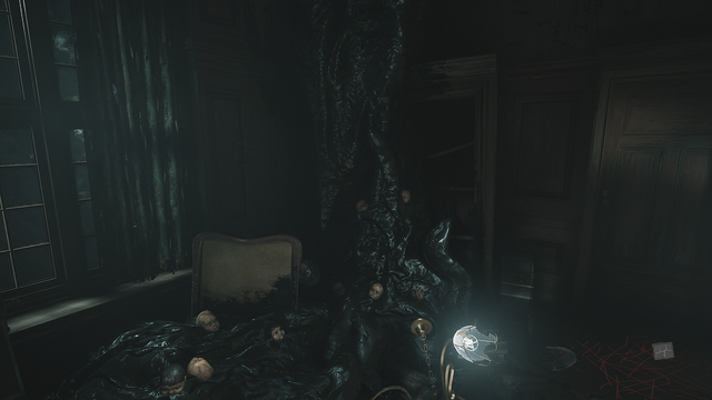 Zrzut ekranu z gry "Layers of Fear" przedstawiający bliżej nieokreślone, zdewastowane pomieszczenie, którego ściany pokryte są ciemno-brązowymi panelami oraz łuszczącą się farbą, odpadającą wraz z tynkiem. Po naszej lewej możemy dostrzec ogromne, brudne okno przez które wpada blade światło księżyca zasłonięte zniszczonymi, podziurawionymi zasłonami w ciemno-zielonym kolorze. Na wprost nas, zarośnięta kolumną czarnej, bezkształtnej masy, spływającej z sufitu, która pochłania i scala ze sobą wszystko, pulsując niczym żyjący organizm będący pasożytniczą naroślą, znajduje się zniszczony regał na książki. Z wnętrza masy, po lewej, wystaje oparcie drewnianego krzesła obitego beżową skórą, po prawej wystaje stolik kawowy z rozbitym, miedzianym żyrandolem świecącą trupio-bladym światłem leżącym na nim. Dodatkowo, na całej długości bezkształtnej, czarnej masy, wystają porcelanowe głowy lalek. Na prawo w tle majaczą dębowe drzwi, przed którymi, na podłodze, ktoś nabazgrał linie przy użyciu czerwonej kredki.
