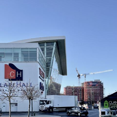 Clare Hall shopping centre, multi-storey glass facade. A building site in the distance. A blue sky above.