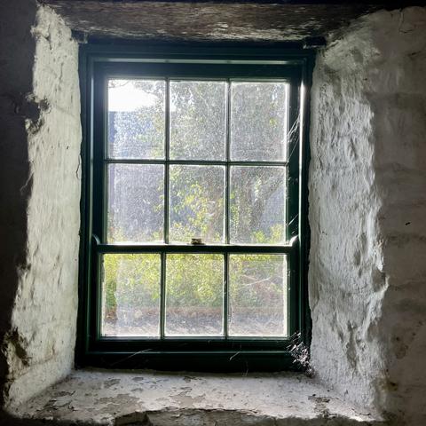 White washed rough stone walls with deep set multi pane green framed window.