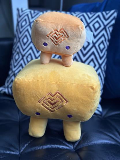 Mama and baby Tracetest plushies. The plushies look like little yellow stools with faces on them, and the Tracetest logo.