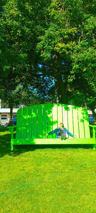 Me sitting on a ginormous green wooden seat with gorgeous green grass and new spring leaves on the trees around me.
