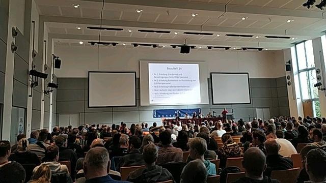 A lot of heads from behind, attending DFV-Symposium and watching the presentation on the big screen.