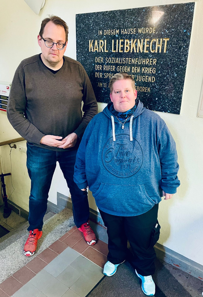 Sören Pellmann und Nancy Frind auf einer Treppe. Im Hintergrund befindet sich eine Gedenktafel für Karl-Liebknecht.￼