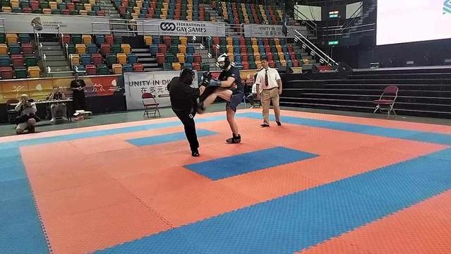 Picture of two martial artists. One in muay thai shorts is kicking another in a black gi, whose leg is also raised. The kick emphasises the musculature of their leg. Both fighters look a little off-balance in the moment of contact, but the muay thai fighter has the advantage of contact in this moment.