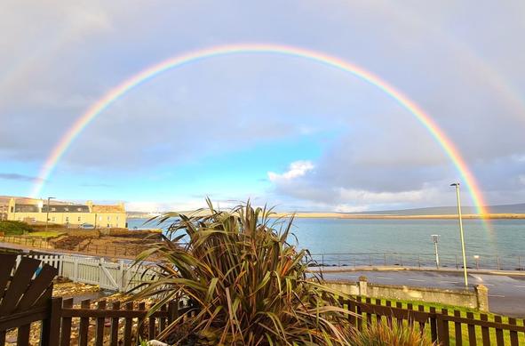 A full rainbow extends across Stromness Harbour.