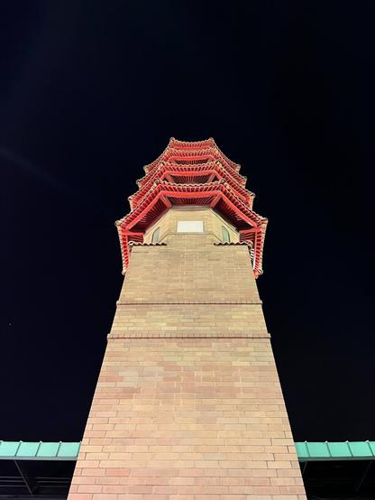 A large beige brick tower with a red and green top in a Chinese style.