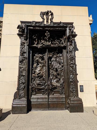 Massive bronze doors leading into hell. The doors are carved with tortured figures inspired by Dante's Inferno.