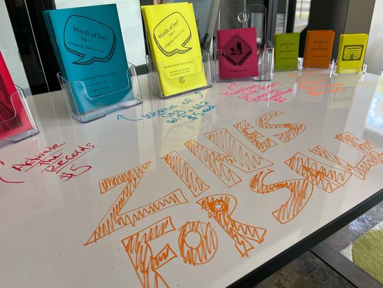 Dry erase table, with various zines and the words, “Zines for Sale”