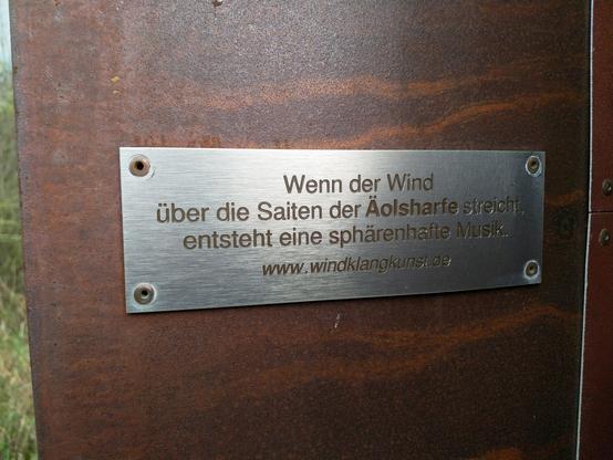 Inschrift der Säulenwindharfe: "Wenn der Wind über die Saiten der Äolsharfe streicht, entsteht eine spärenhafte Musik. www.windklangkunst.de