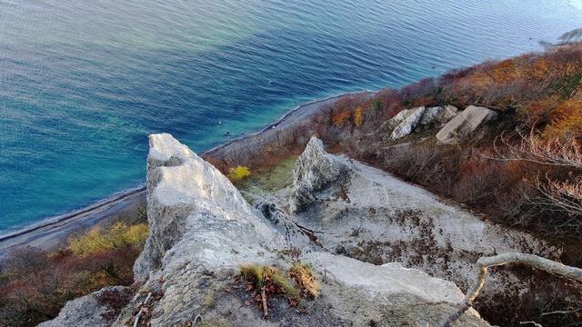 Blick von oben auf die Steilküste über der Ostsee. Der Hang besteht aus KreidefelsWasseren, umrahmt von herbstlichen Laub und das  der Ostsee schimmert türkis.