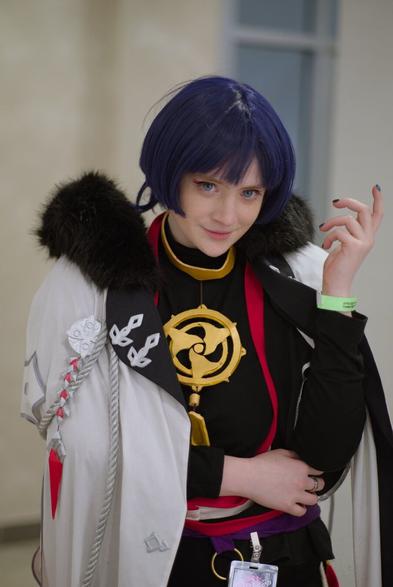 A half-body portrait of a girl with bobcat-styled blue hair wearing black long-sleeved chinese-style robe with red ornament and kind of white coat with black collar made of short fur. On her chest there is big golden-colored pendant in form of 3 turned curved blades. Her left elbow pressed to her side, her left hand points upwards, her right hand holds her left elbow. Her head is tilted slightly forward, her eyes are blue, she smiles a bit looking to the camera.