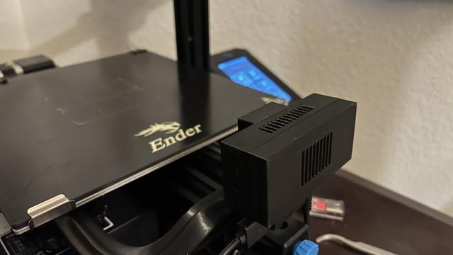A photo of the rev 2 case from the fan side with my Ender 3 printer and its control panel in the background. The control panel is a blue tinted LCD screen and control knob.