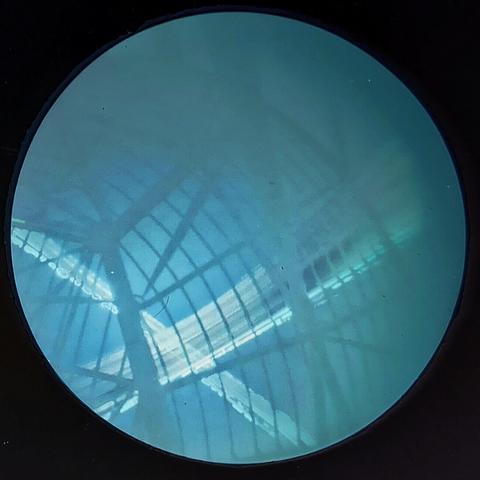 A blue tinted view of the underside of a radiotelescope dish, looking up at the sun's path. There are two sets of paths, crossing at close to 90 degrees. The sun's paths are almost white.