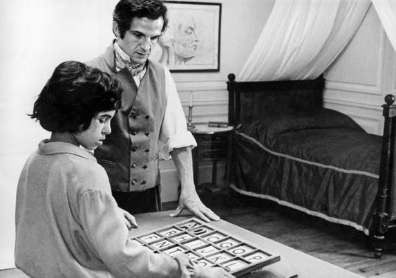 Victor, the Wild Boy of Aveyron (Jean-Pierre Cargol), reads letters from a board under supervision of Dr. Jean Itard (Truffaut).