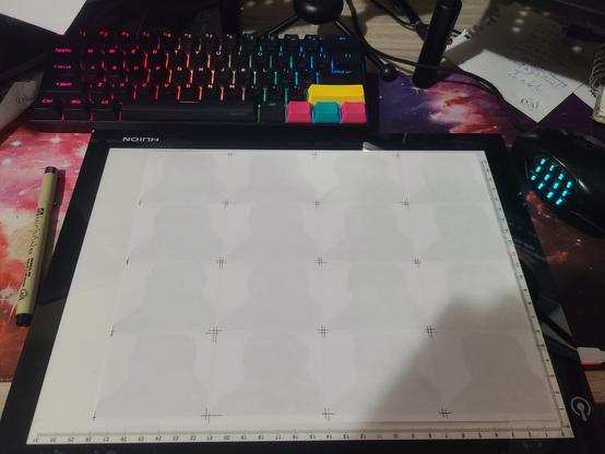 A light board with white printer paper to it, guides jotted to replicate the 16 cells from before. A Micron 03 pen rests on the desk next to it