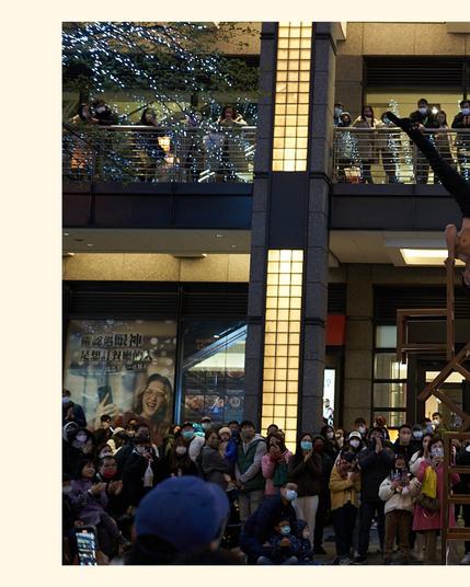 An athlete street performer doing a handstand on top of a pillar of chairs. A crowd gathered around him, watching in awe.