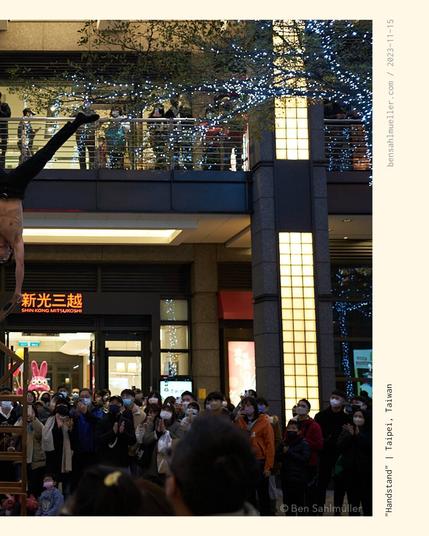 An athlete street performer doing a handstand on top of a pillar of chairs. A crowd gathered around him, watching in awe.