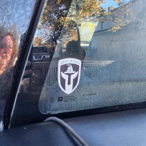 Black and white sticker on back window of black truck with Liberty or Death written on top.
What looks like a white robed figure hands up to sky and where the head should be is the oathkeepers snake symbol.