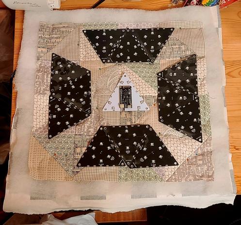 Four groups of three black tiles are placed on the smaller prototype 35 cm #quilt square in tesselated groupings. 

The solidly packed groups of three are at the compass point positions. This smaller prototype will resemble the controller board clock face on the full size quilt panel.