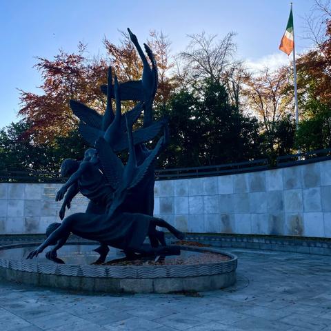 Bronze monument depicting Children of Lir transforming from rising swans to fallen humans. A tricolour behind with trees.