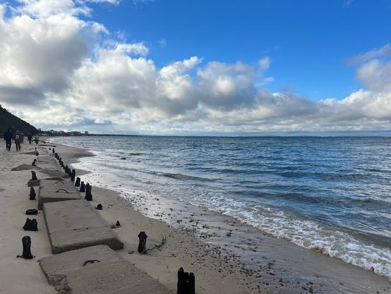 Am Strand mit Betonblöcken um den Sand zu halten. Blauer Himmel mit weißen Wolken
