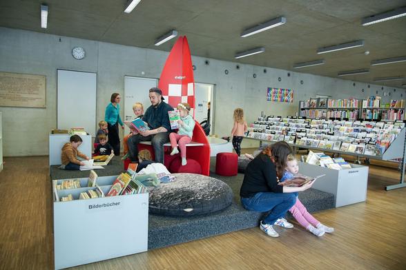 Eine Bibliothek, in der viele Kinder von Erwachsenen vorgelesen bekommen.