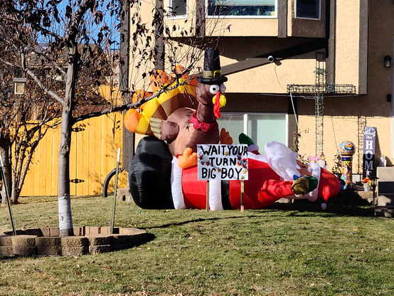 Blow-up turkey sitting atop a blow-up Santa Claus, with a sign saying "wait your turn big boy."