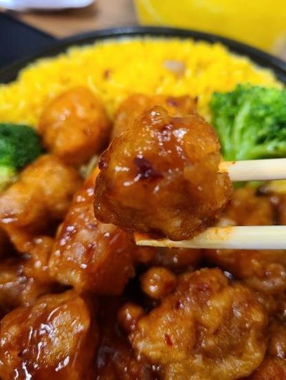 Photograph of a bowl of General Tso's Chicken. Chop sticks are grabbing a piece of meat.