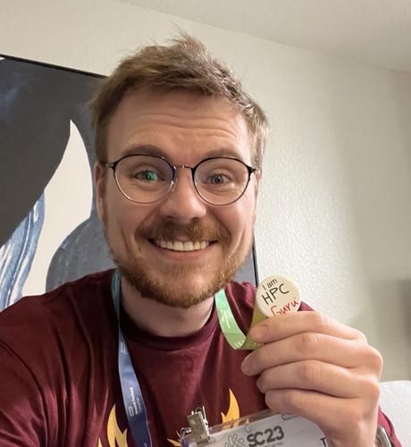 Selfie of a mid to late twenties white man with blond hair, a red beard and glasses

In Their hand is a pin hanging from a conference badge.
The pin says “I Am HPC Guru”