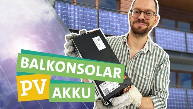 Thumbnail zeigt einen weißen Mann mit dunklem Bart und Brille, der ein beige-grün längs gestreiftes Hemd und Arbeitshandschuhe trägt und eine schwarze, rechteckige Batterie lächelnd in die Kamera hält. Die Batterie ist etwa 40 cm hoch und 20 cm breit, die Tiefe ist schwer zu erkennen. Im Hintergrund sind Solarmodule an Balkonen zu sehen. Im Vordergrund die Wörter "Balkonsolar PV Akku", grün bzw. gelb hinterlegt.