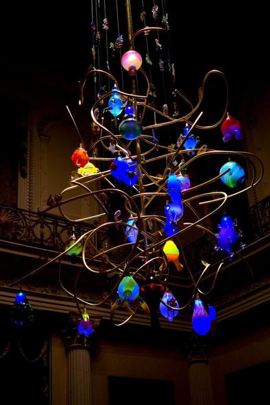 A huge chandelier, 5 meters (about 16 feet) wide and much higher, maybe 10 meters? The chandelier is made of curved rods in a kind of messy knot, with blown glass figures in blue, orange, yellow, green and pink (mostly blue) hanging in the chandelier.