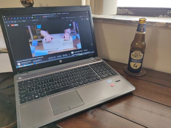 Picture of my HP ProBook 4540s laptop running Fedora 39 MATE with Firefox focused on YouTube with Macintosh Librarian showcasing the PowerComputing PowerCenter 132 desktop PowerPC Macintosh clone. To the right of it on a coaster is a bottle of Birrificio Angelo Poretti Premium Lager beer.