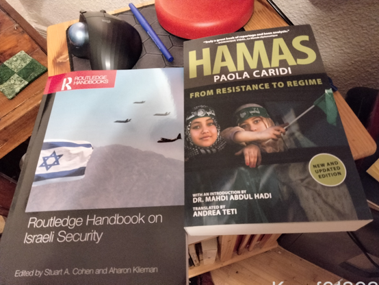 Routledge Handbook of Israeli Security (a flag, three jets, and a prop-driven plane) & Hamas: From Resistance to Regime, New and Updated Edition (two girls in non-steteotypical keffeyehs bound by green headbands with Arabic script and a Hamas emblem featuring Al-Aqsa, an AK-47 (?), and a pine tree). The one with startling green eyes is holding a small green flag out of frame.