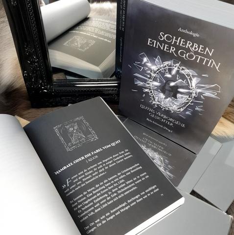 Cover von Scherben einer Göttin und aufgeschlagenes Buch auf der Startseite der Kurzgeschichte von J. Kilior, schwarze Buchseite.