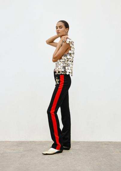 An image from the Rabanne H&M collection. Model wearing a singlet made of metal paillettes, and a striped trouser (in navy with red stripe).