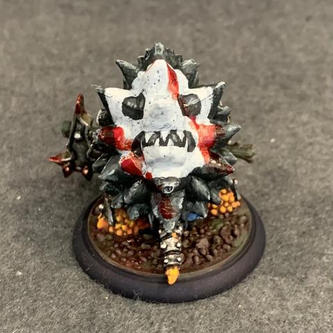 The back of the mini. Stout bipedal turtle-person in heavy plate armor and a giant black shell with a white skull painted on the back. He holds a giant blood-smeared two handed axe. He has rough orange skin, and he glares with pupil-less eyes and an open mouth. Blood is also smeared across his face, armor, and shell.