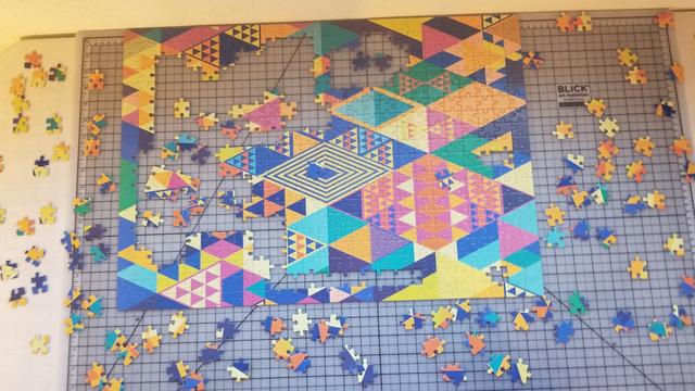 An incomplete 500 piece jigsaw puzzle of two dimensional triangles and diamond shapes in primary, pastel,  and neon colors.